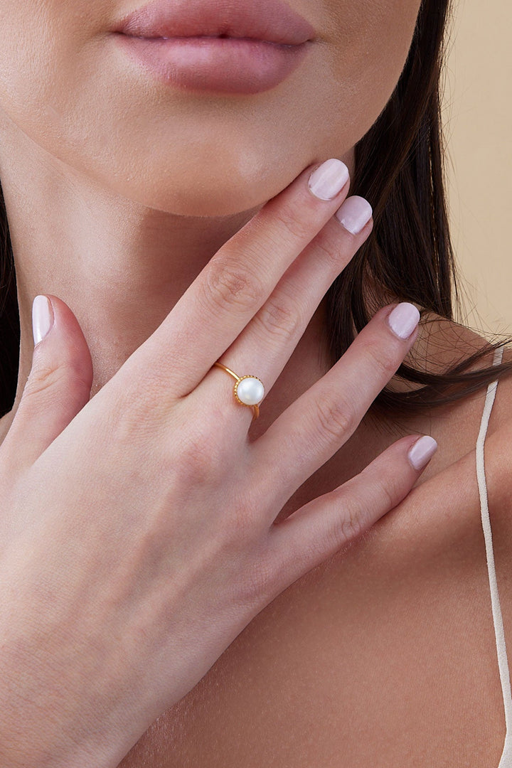 Woman with hand on neck against a beige background with pearl ring gold plated 