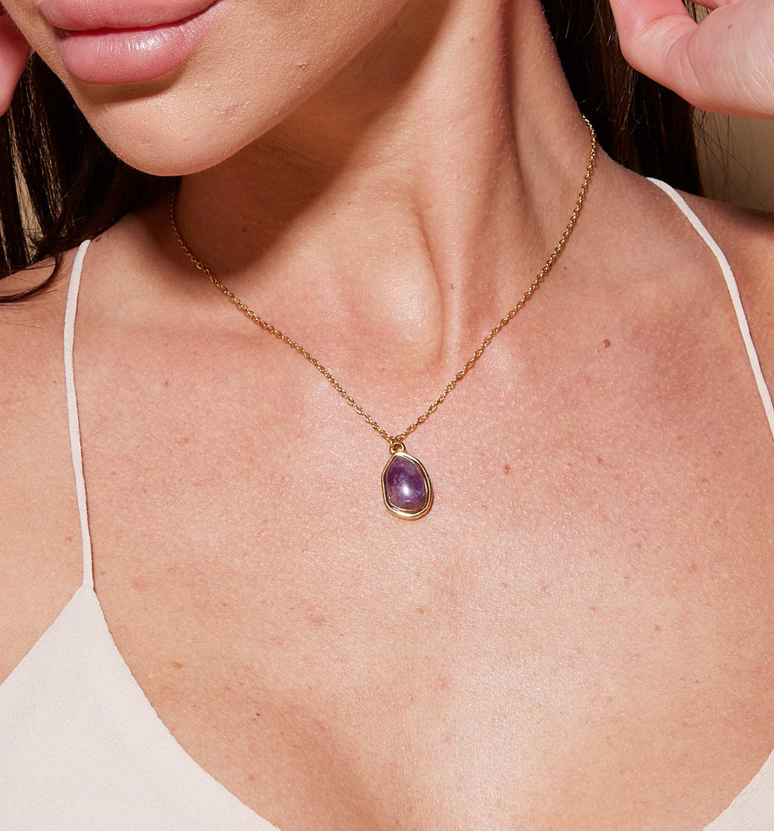 Woman wearing a necklace with a purple pendant against a beige background