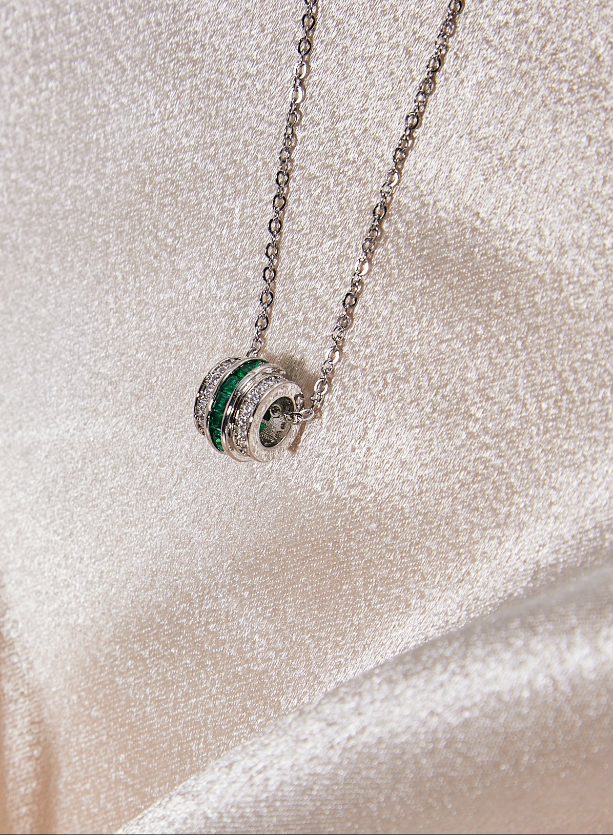 Silver necklace with a green gemstone pendant on a soft fabric background