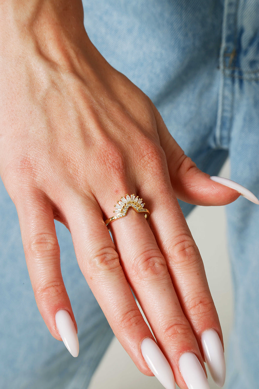 Hand wearing a gold ring with gemstones against a denim background