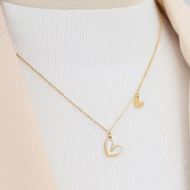 A gold necklace with two heart pendants, displayed on a white ribbed surface.