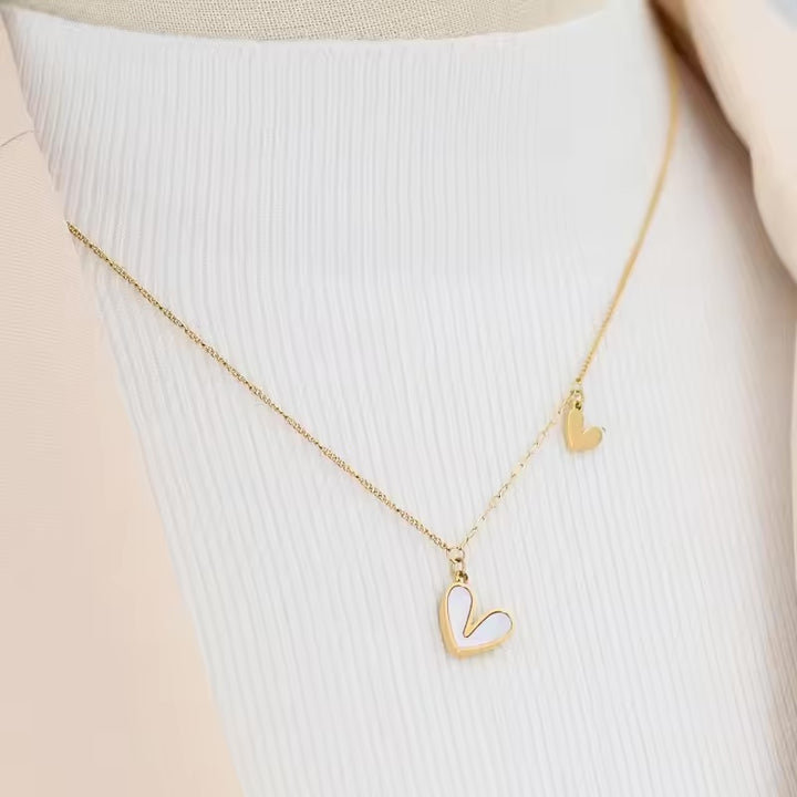 A gold necklace with two heart pendants, displayed on a white ribbed surface.